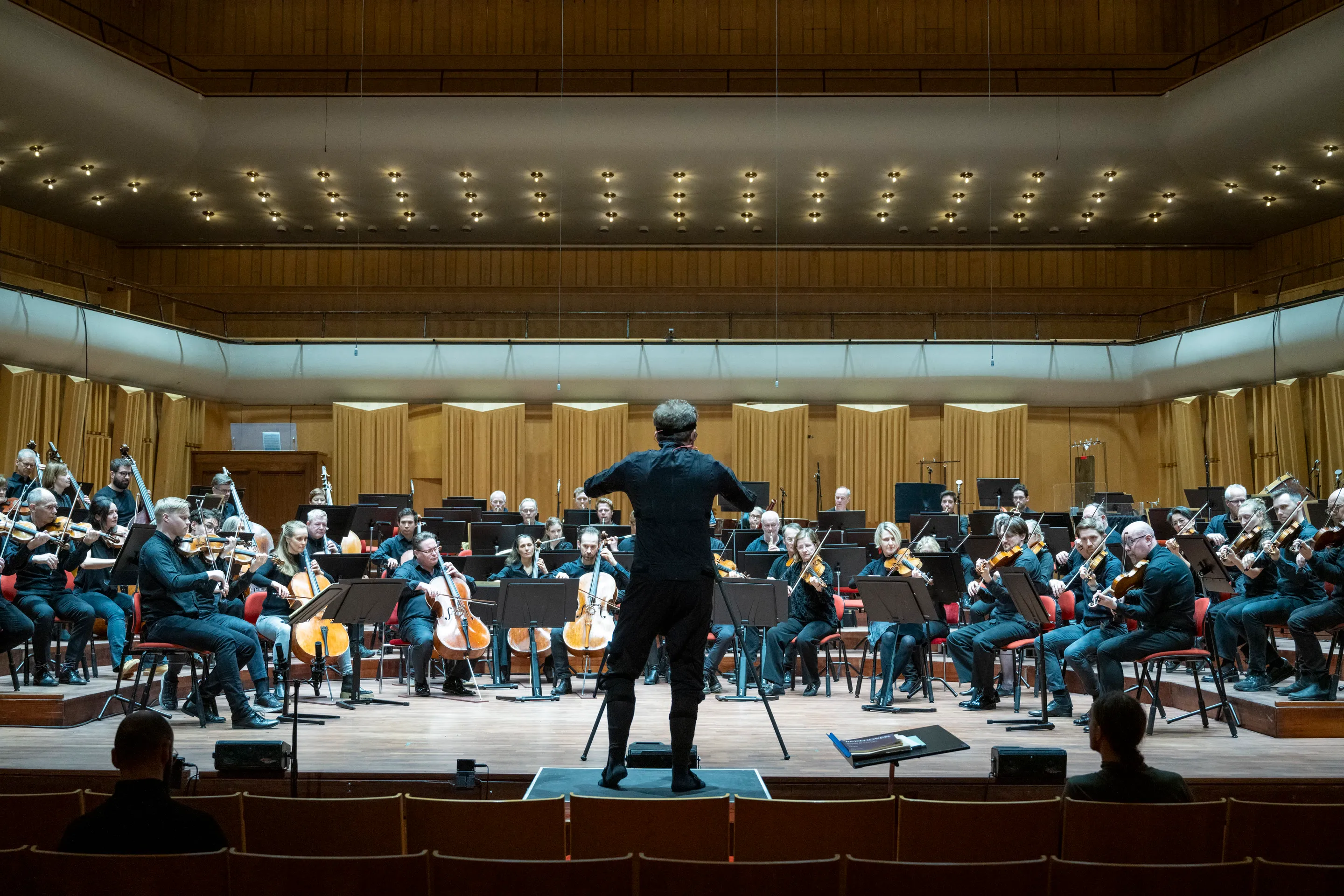 The conductor leading the full orchestra in the concert hall during the recording session