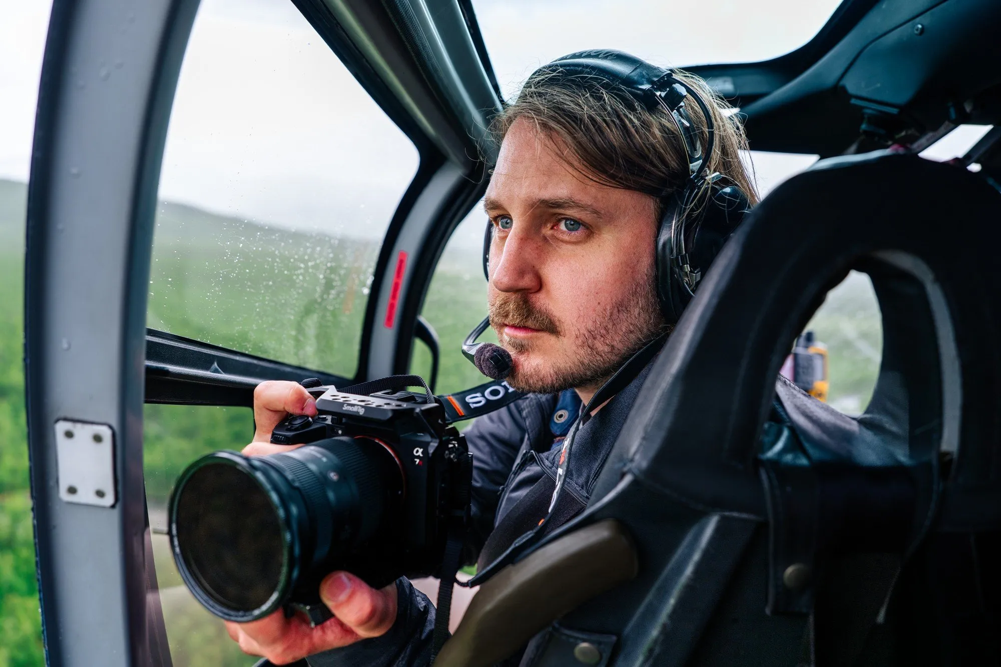 Fredrik Edström i en helikopter med headset filmar genom det öppna fönstret