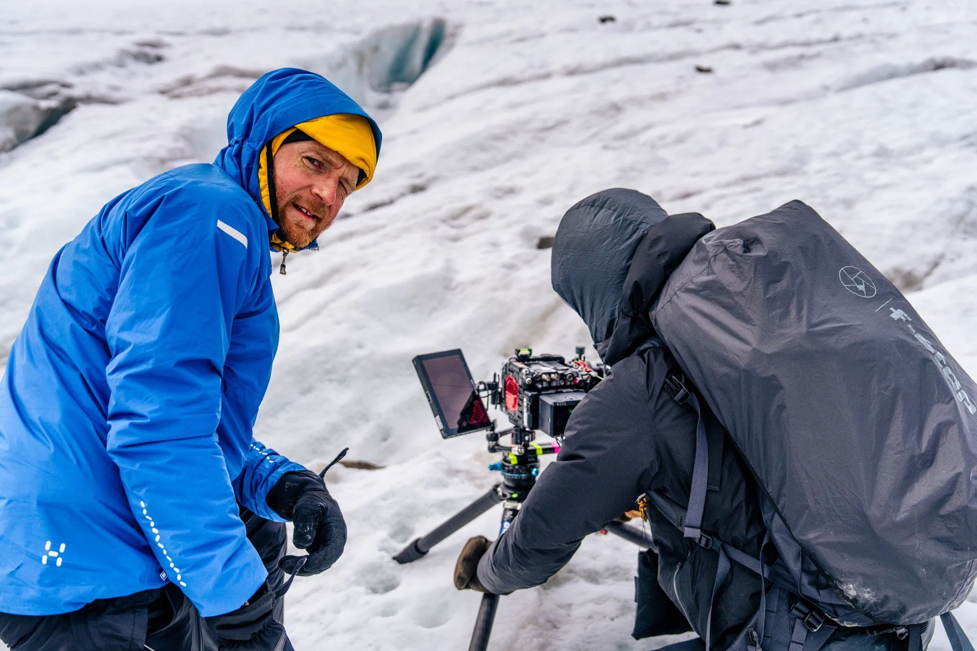 Martin Edström i blå jacka tittar mot kameran medan Oliver Akermo filmar bland sprickorna på Storglaciären