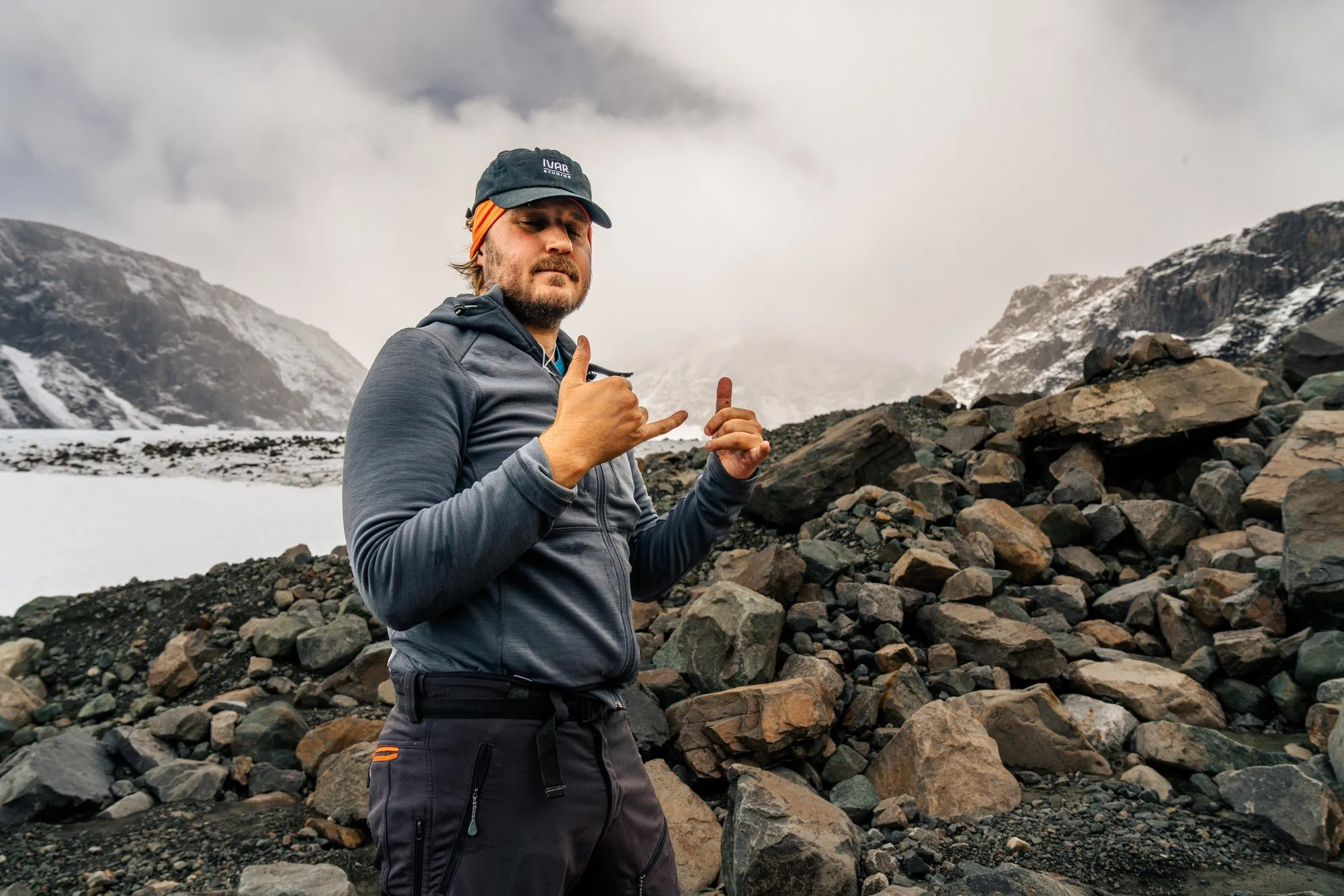 Fredrik Edström i grå fleece och keps på en stenig morän, med en glaciär bakom sig
