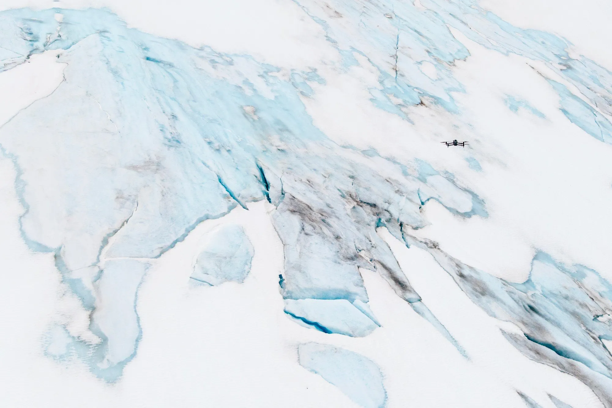 En liten drönare flyger över sprucken glaciäris med blå sprickor