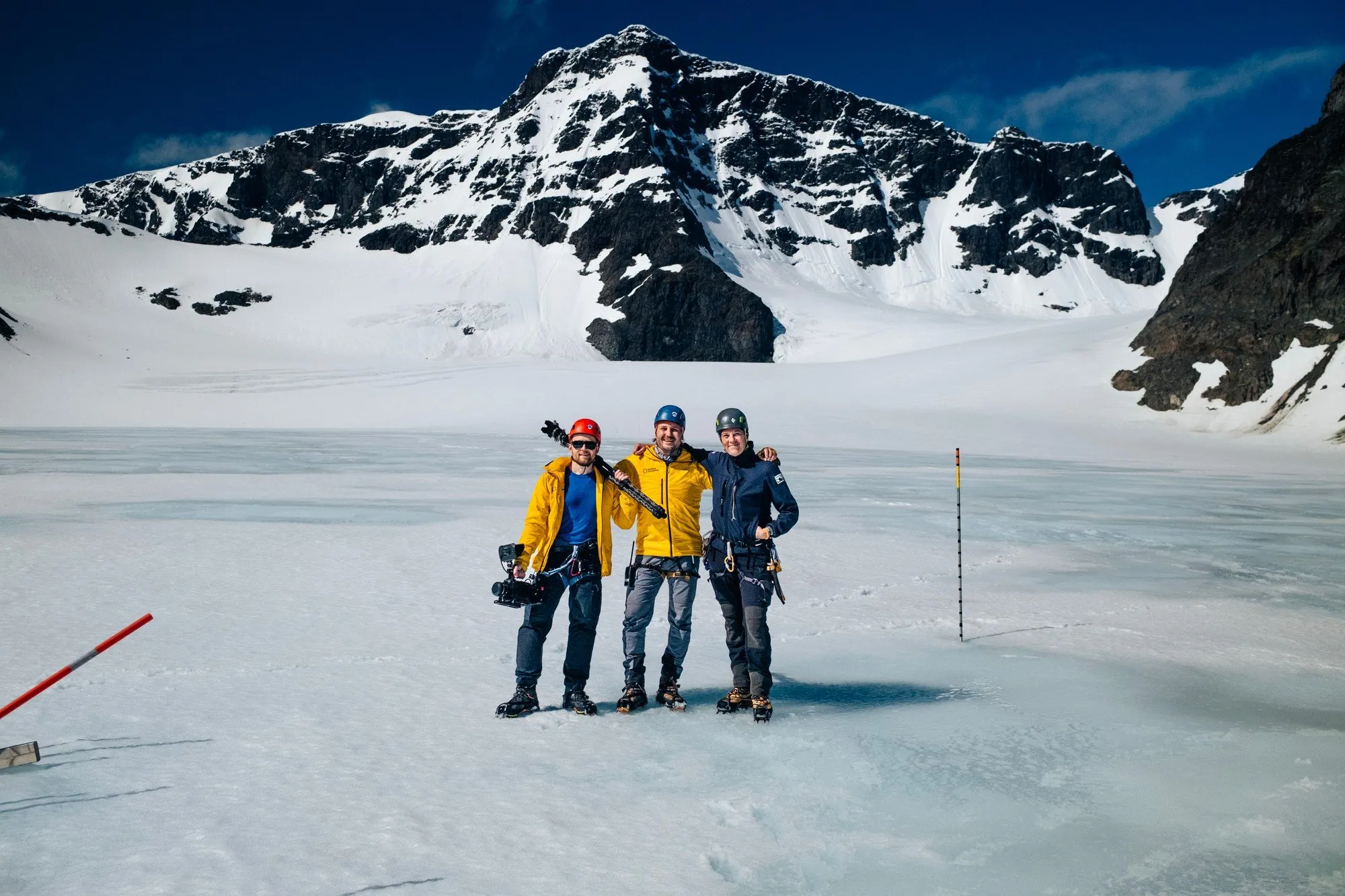 Tre personer i vinterkläder på Storglaciären, bland dem Nina Kirchner, med kamera och stativ och en snötäckt topp bakom sig