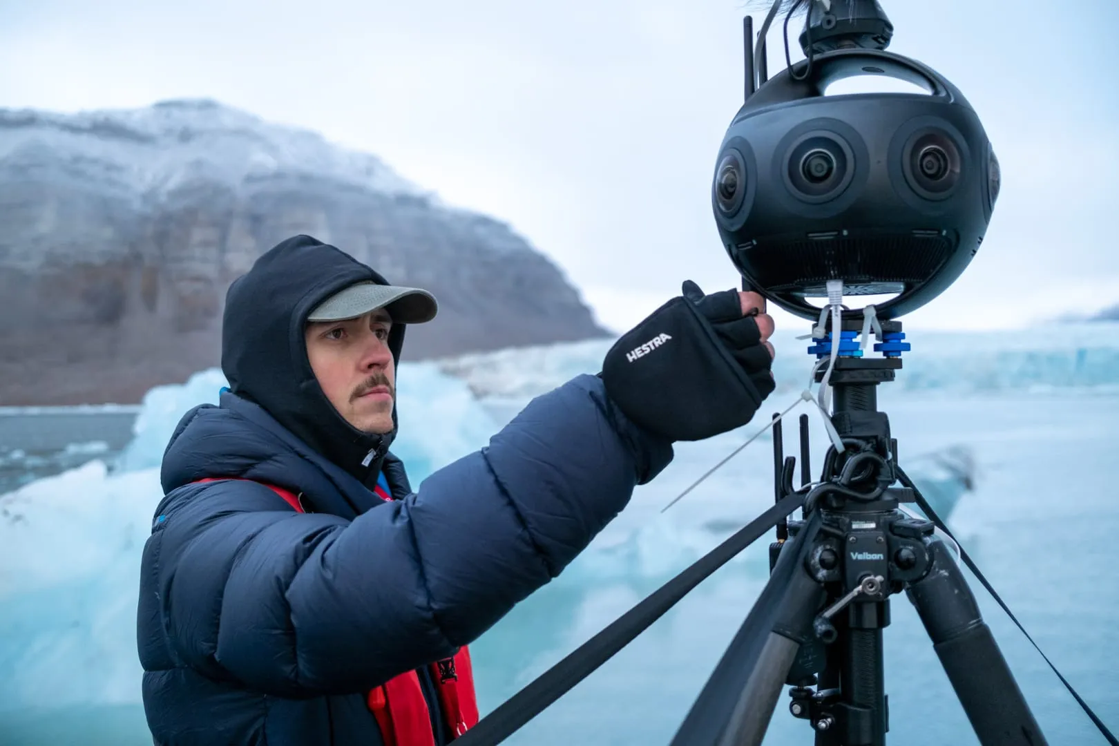 A crew member adjusting a 360° camera in front of a glacier in Svalbard