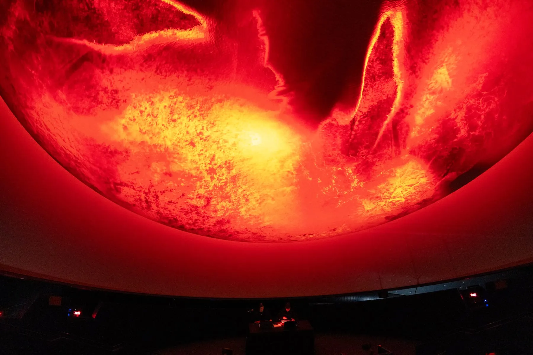 A red fulldome projection above two operators at a control desk