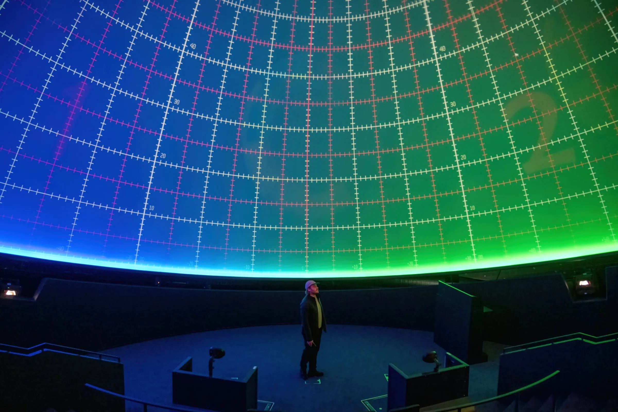 A person standing under a planetarium dome lit with a projected grid